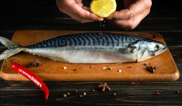 chef adds fresh lemon juice raw mackerel fish before cooking with ingredients aromatic spices