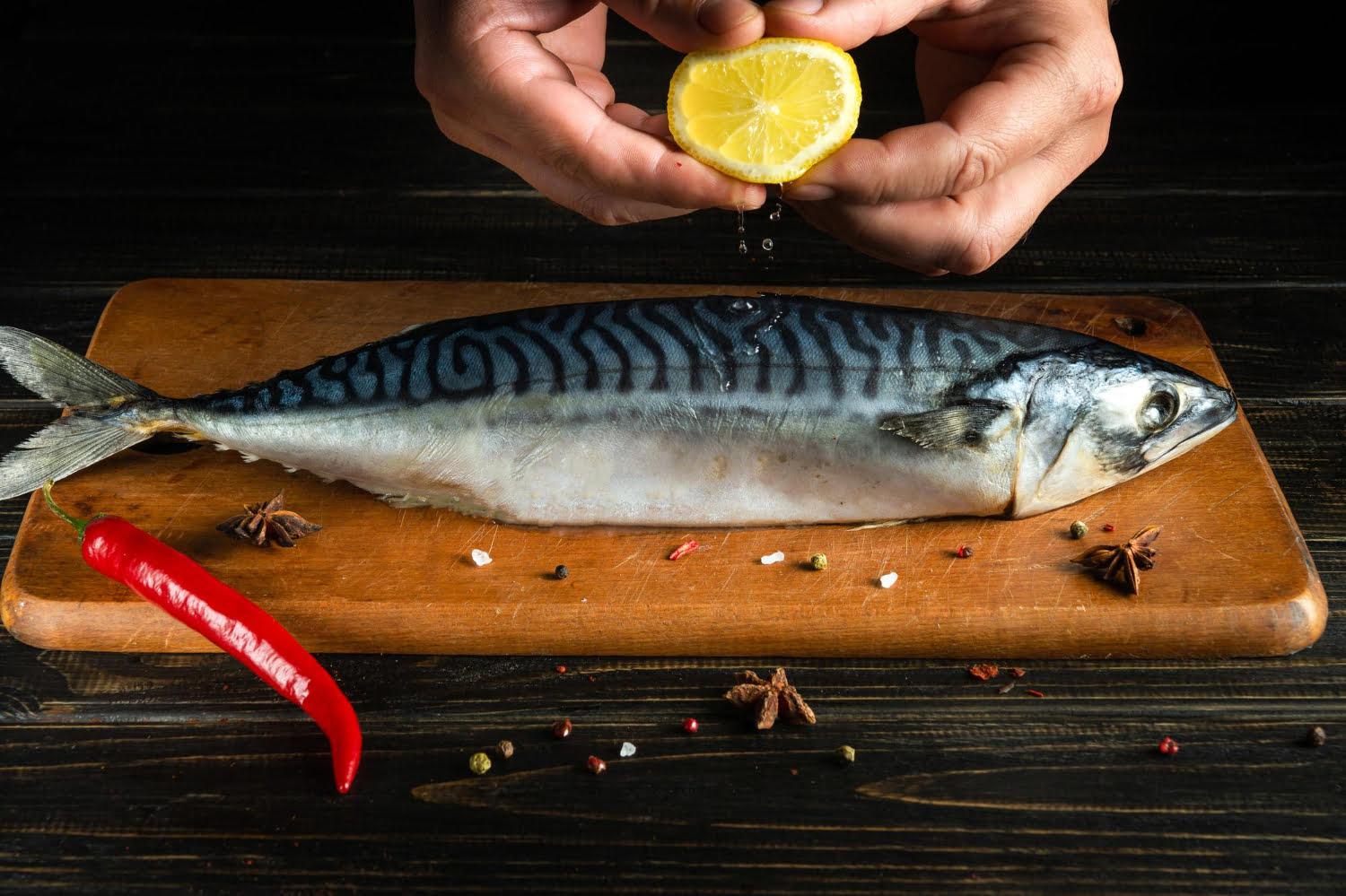 chef adds fresh lemon juice raw mackerel fish before cooking with ingredients aromatic spices