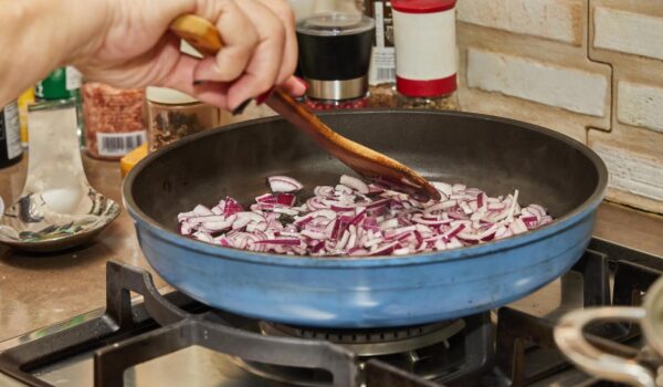 chef stirs purple onions into frying pan gas stove