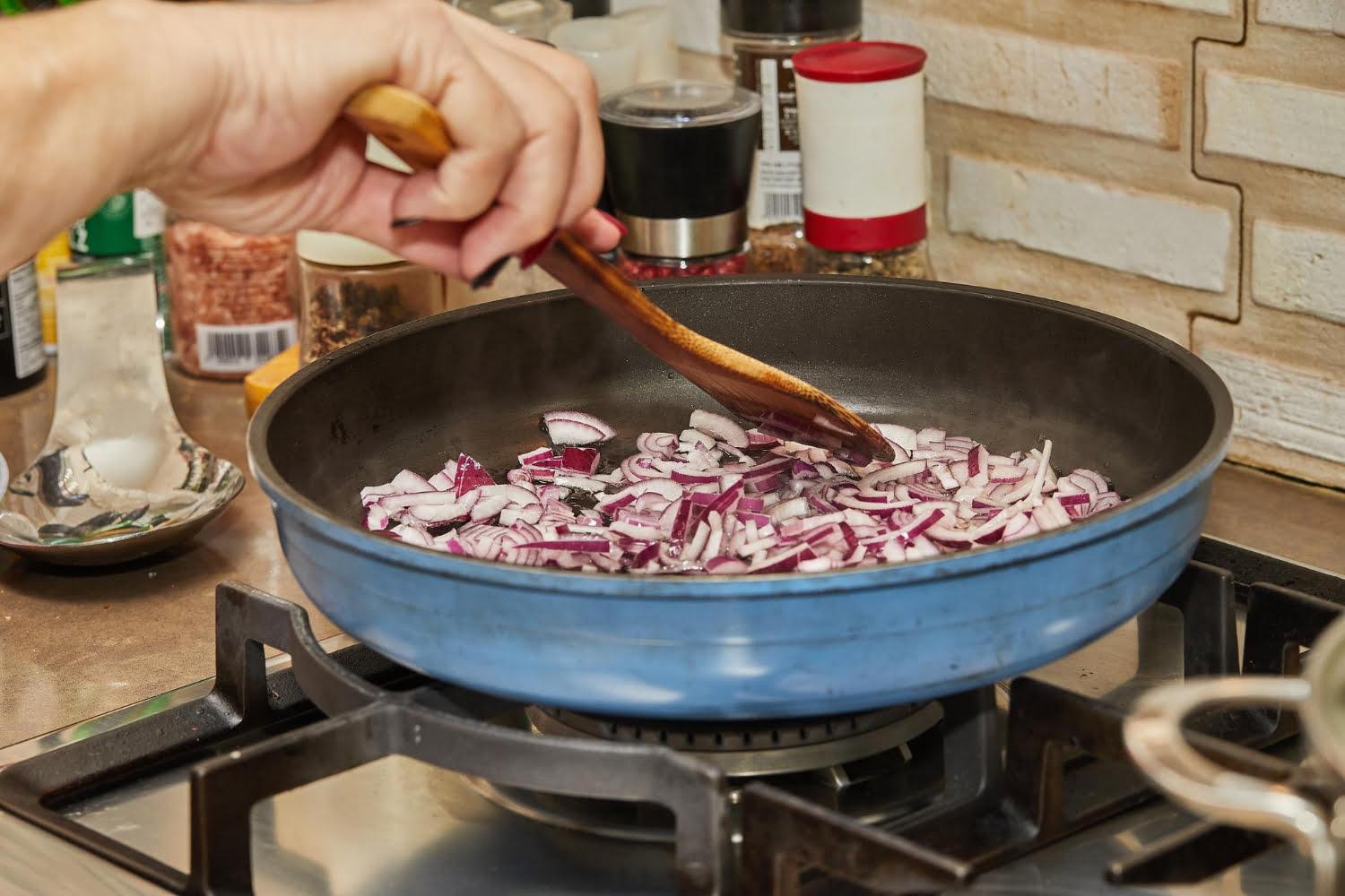 chef stirs purple onions into frying pan gas stove