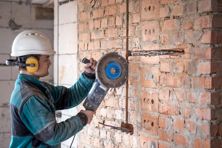 a professional builder in work clothes works with a cutting tool.